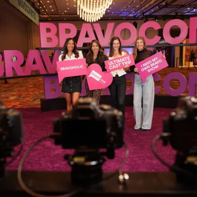 Fans hold up signs at the pink BravoCon photo booth as cameras capture the moment
