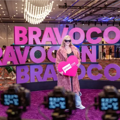 A fan holds a heart-shaped sign in front of giant pink BravoCon letters